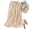 Beige wide leg cotton pants with embroidery and drawstring waist laid flat next to accessories