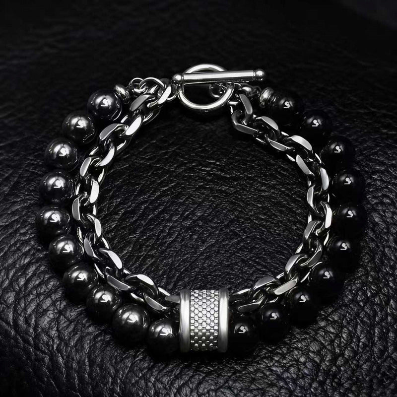 Close up of a men's bracelet with a gunmetal chain and dark stone beads on a black leather background