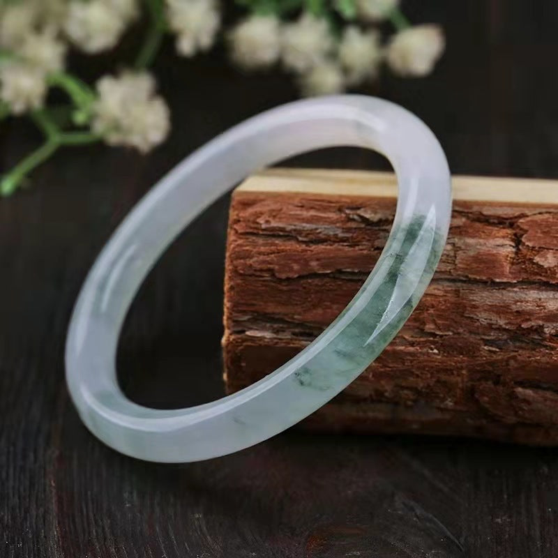 A translucent white and green jade bangle resting on a wooden block