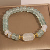 Close up of a light blue abacus bead bracelet with a central white carved charm on a beige background