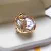 Close up of a gold tone ring with a large white baroque pearl and leaf detail