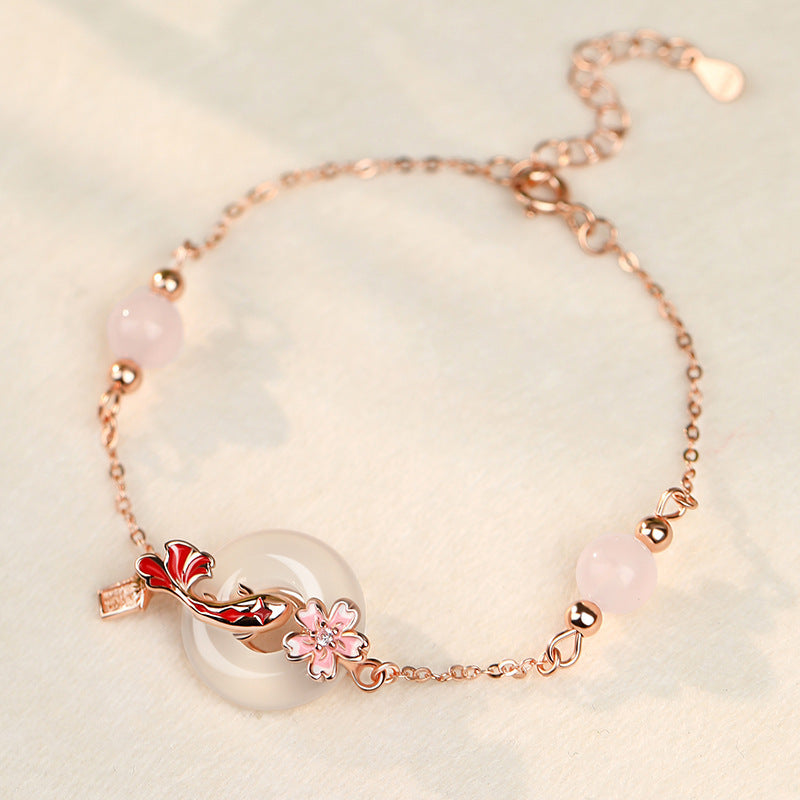 Close up of a rose gold tone silver bracelet with a white jade donut, red koi fish and pink beads