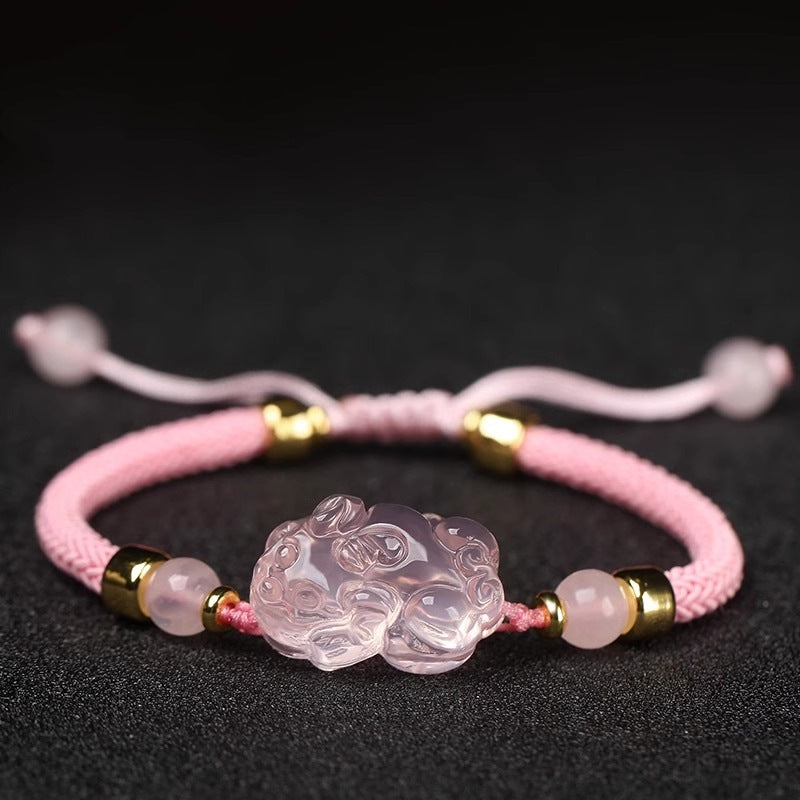 Close-up of a pink crystal Pixiu charm on a braided pink cord bracelet