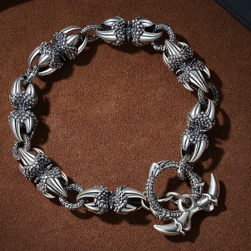 Silver-tone copper bracelet with dragon claw links and a vajra charm on a dark surface