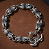 Silver-tone copper bracelet with dragon claw links and a vajra charm on a dark surface