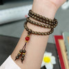 Close-up of a multi-wrap wooden mala bracelet with 108 beads and a red accent bead worn on a wrist.