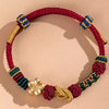 Close-up of a red hand-woven cord bracelet with gold and blue knot details and a flower charm