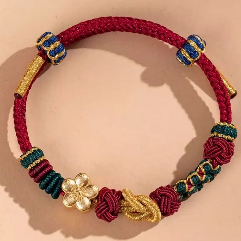 Close-up of a red hand-woven cord bracelet with gold and blue knot details and a flower charm