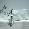 Light green canvas clutch purse with white lotus flower embroidery and a matching tassel charm.