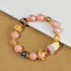 Close-up of a pink glass bead bracelet with gold accents and a white fox charm on a textured surface