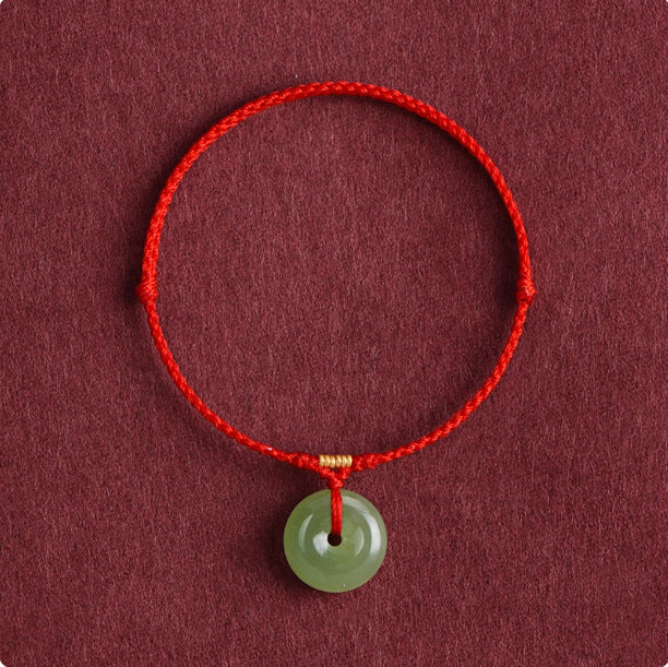 Green jade peace buckle hanging from a thin red braided cord with a gold bead