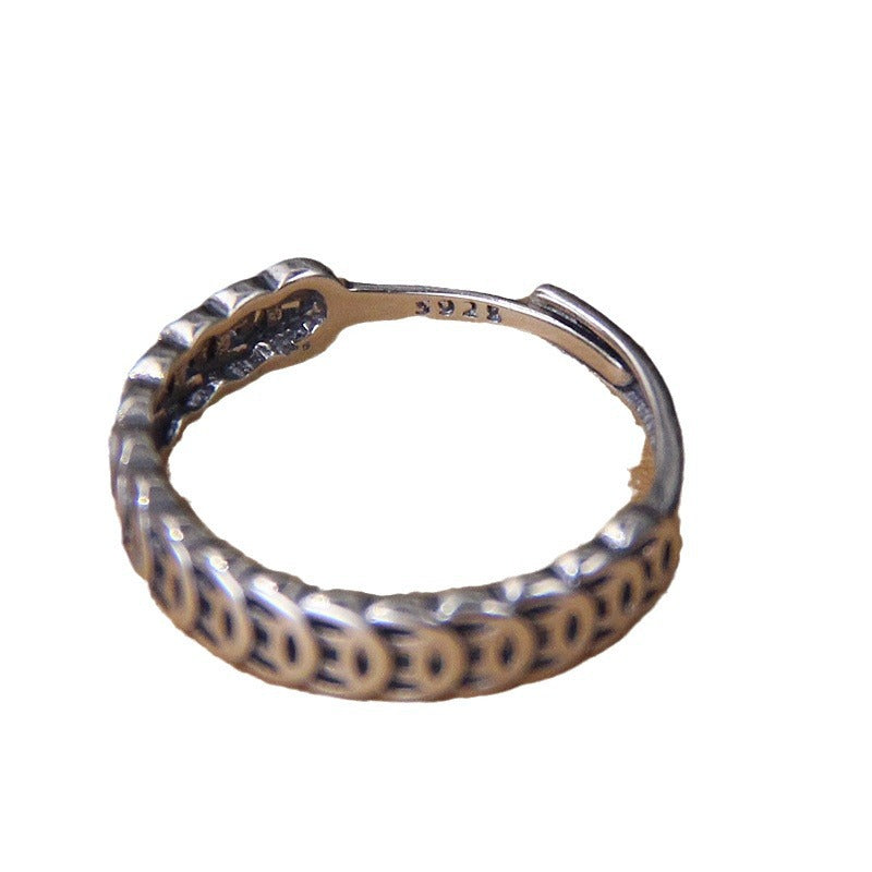 Close up of a silver ring with a chain of coin shapes on a dark surface