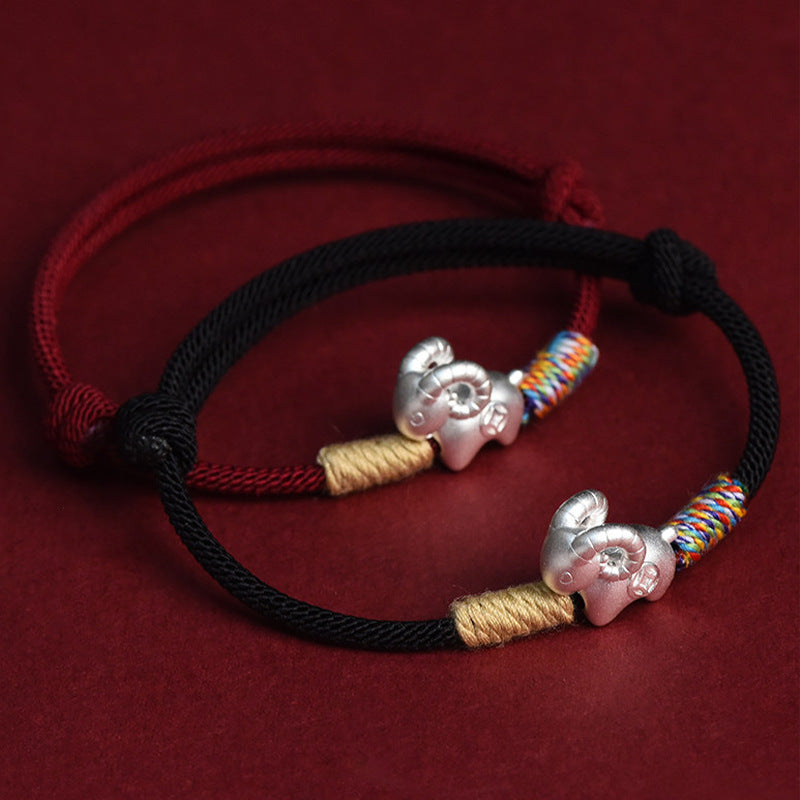 Silver-tone sheep charm on a red string bracelet against a dark background