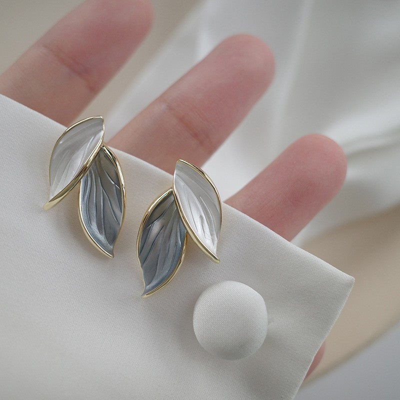 Close up of blue and white leaf shaped stud earrings on a hand