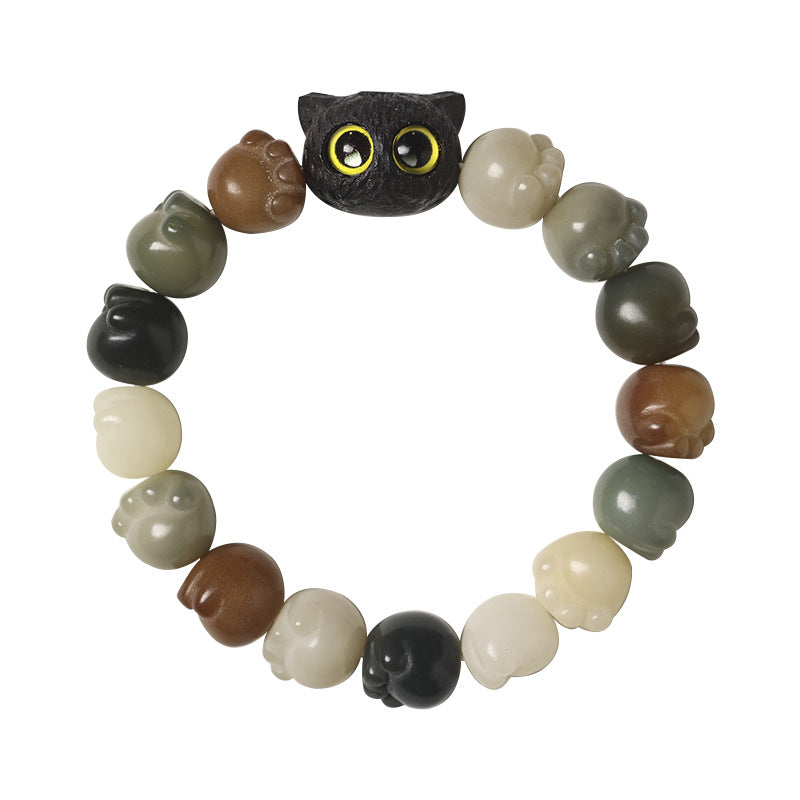Close up of a bodhi seed bracelet with a black cat head charm and hanging tassel on a wooden surface