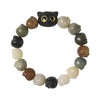 Close up of a bodhi seed bracelet with a black cat head charm and hanging tassel on a wooden surface