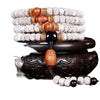 A coiled bracelet made of white speckled bodhi seeds with orange and black accent beads resting on a wooden stand.