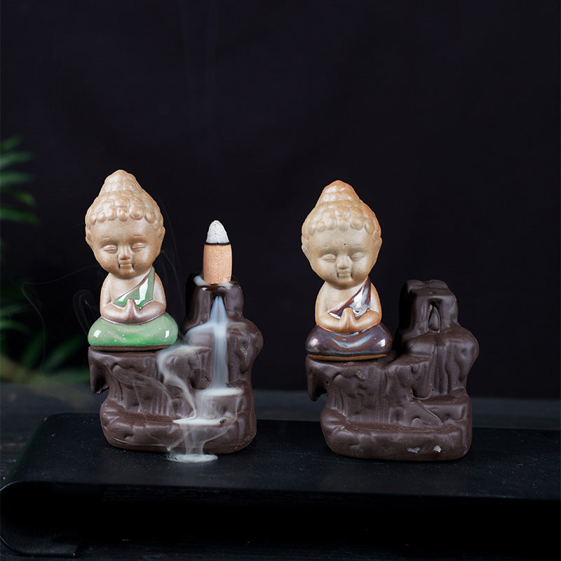 Two ceramic incense burners with Buddha figures, one green and one brown, showing backflow smoke.
