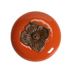 Orange ceramic persimmon incense burner with a brown top holding a stick of incense on a woven mat.