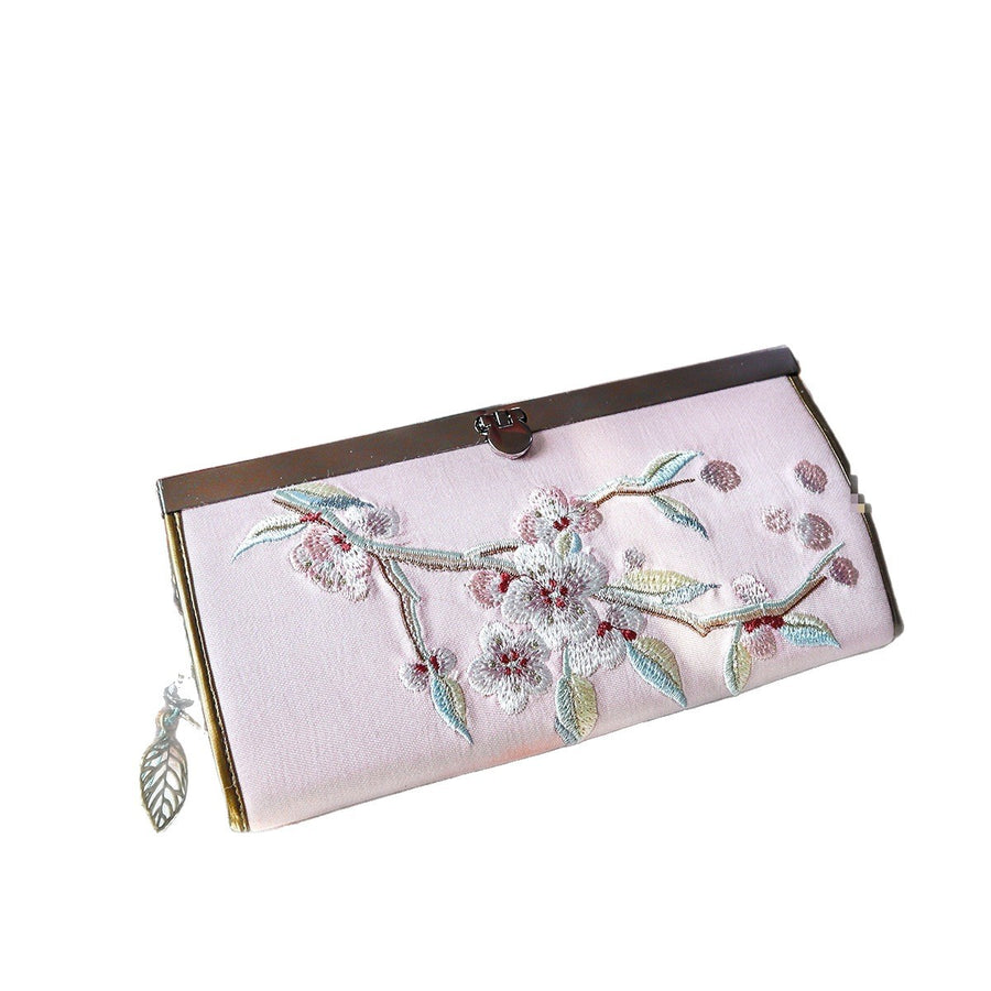 Close-up of a pink velvet wallet with white and green floral embroidery and a metal clasp