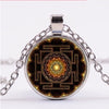 Close up of a round pendant with a golden Sri Yantra geometric pattern inside a glass dome on a silver chain