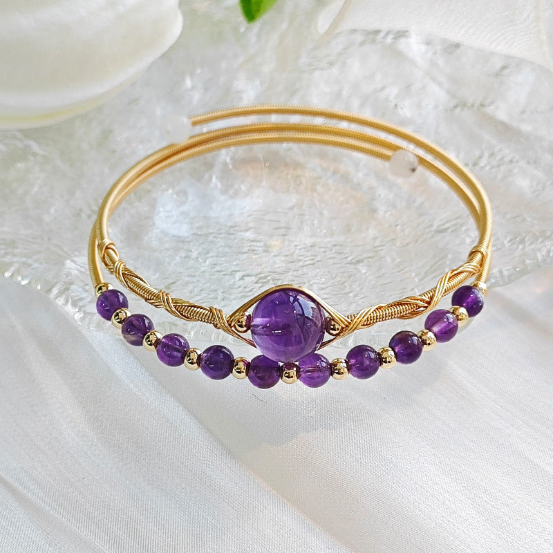 Close up of a gold tone wire wrapped bangle bracelet with purple amethyst beads and a central stone