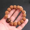 A hand holding a brown bodhi seed bracelet with a dark carved Pixiu bead.
