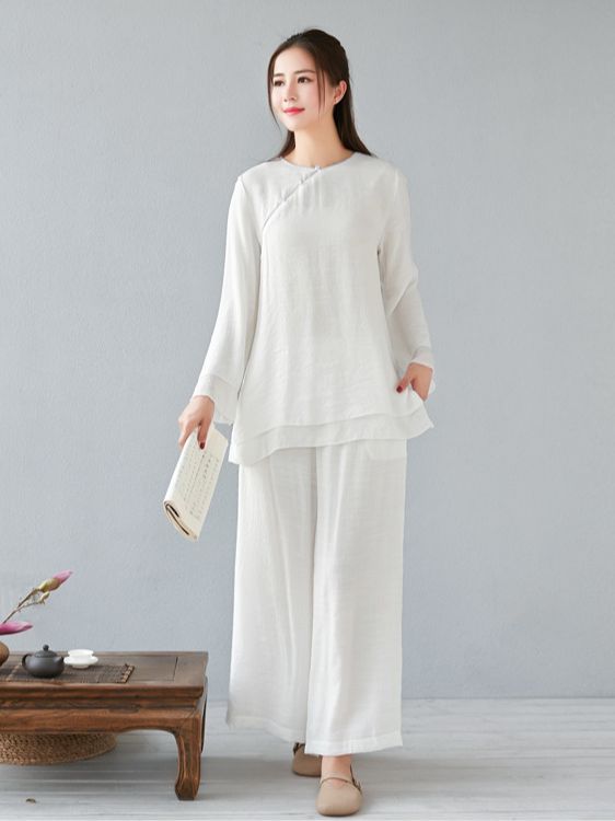 Woman wearing a white long sleeve linen top and wide leg pants standing next to a tea table