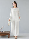 Woman wearing a white long sleeve linen top and wide leg pants standing next to a tea table