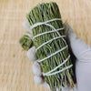 Hand holding a bundle of dried green sage leaves tied with white string