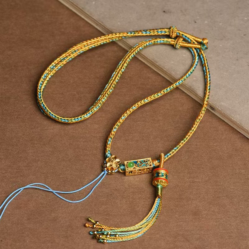 Close up of a multicolored handmade braided necklace with a gold-tone pendant and tassel