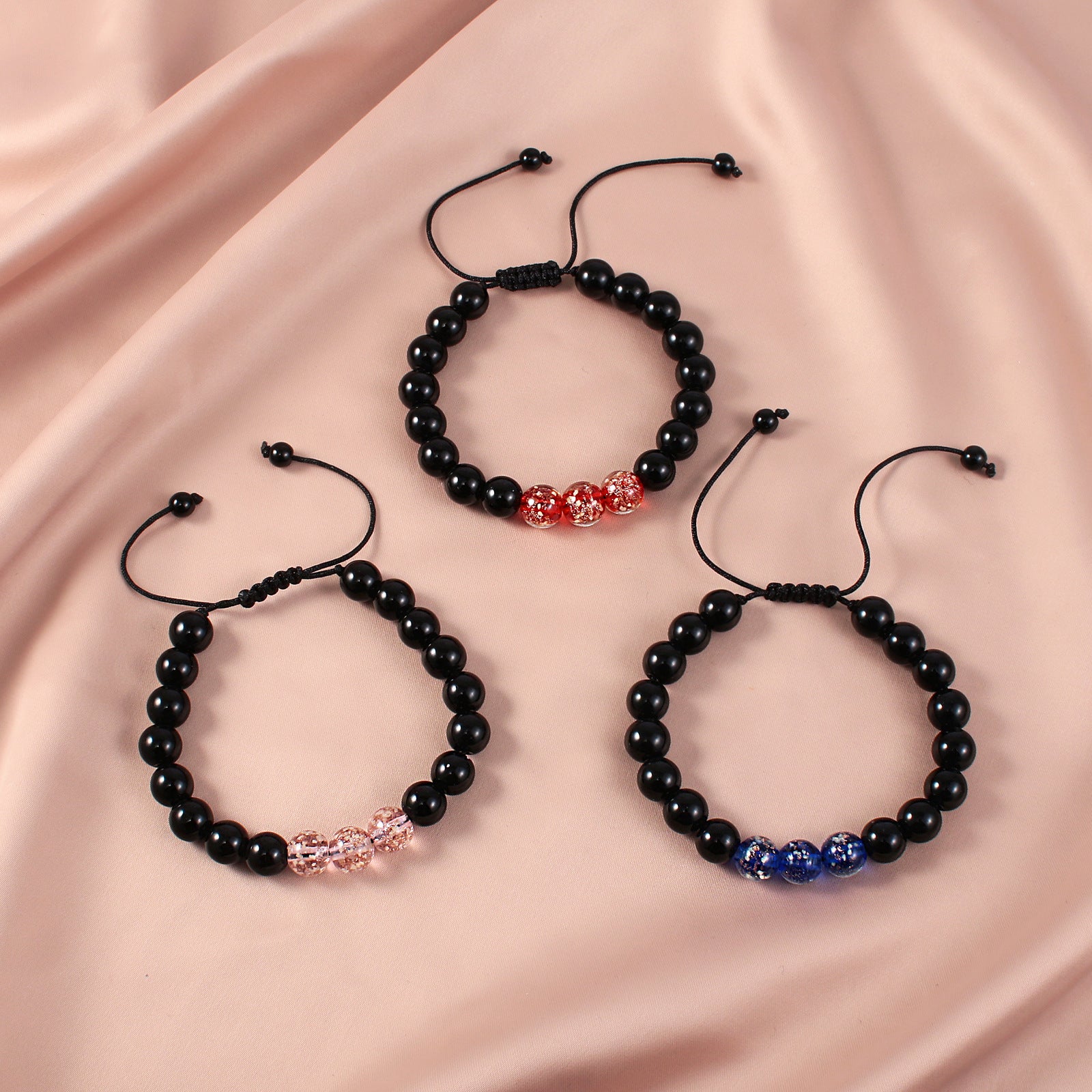 Three black beaded bracelets with red, pink, and blue glowing accents on a pink fabric background