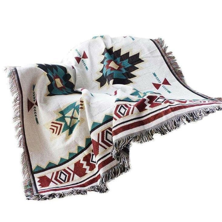 A white cotton throw blanket with red and teal geometric patterns draped over a surface