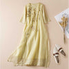 Light yellow midi dress with floral embroidery laid flat on a beige background