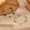Gold tone bracelet with green rutilated quartz beads, star charm and infinity link on beige fabric