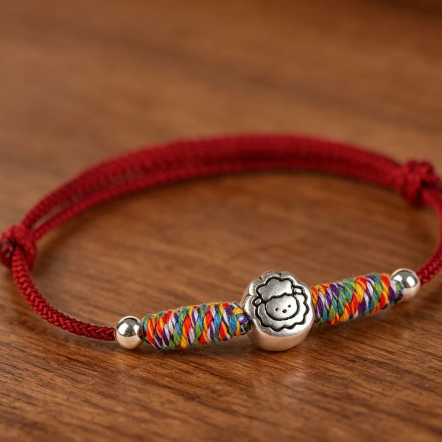Close up of a red string bracelet with a copper goat charm and rainbow colored thread accents on a wooden surface.
