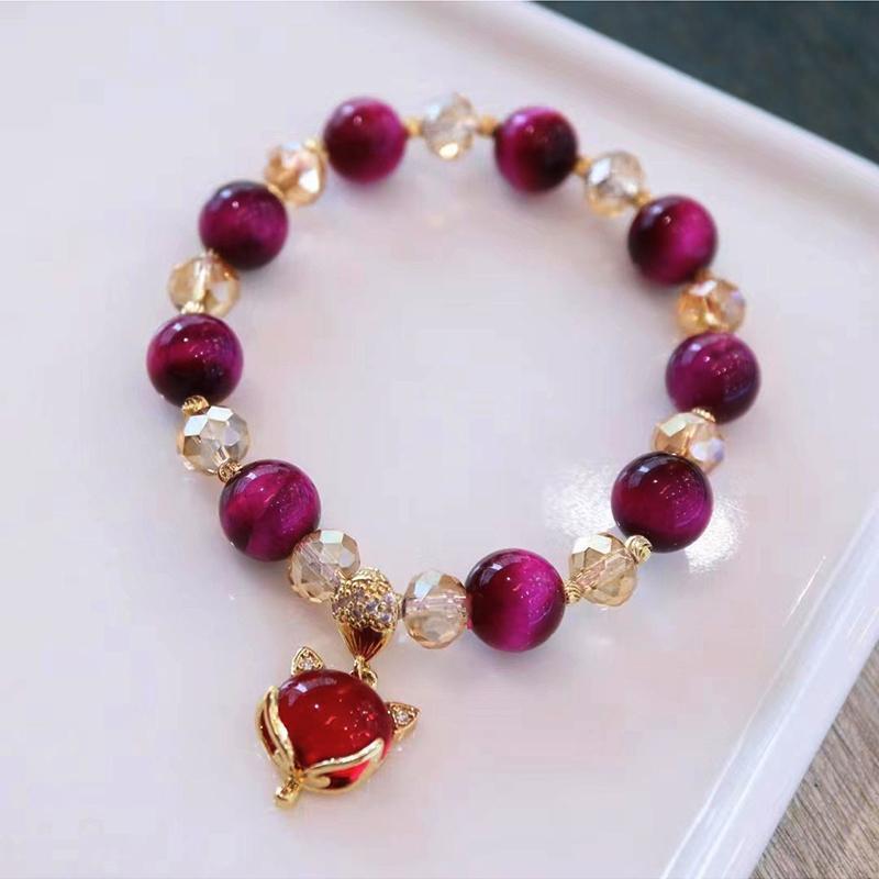 Rose red tiger eye beaded bracelet with a gold tone fox charm on a white tray