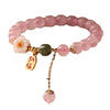 Close up of a pink crystal beaded bracelet with a white flower charm and gold tassel