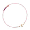 Close-up of a wrist wearing a thin pink and red beaded bracelet with a gold clasp