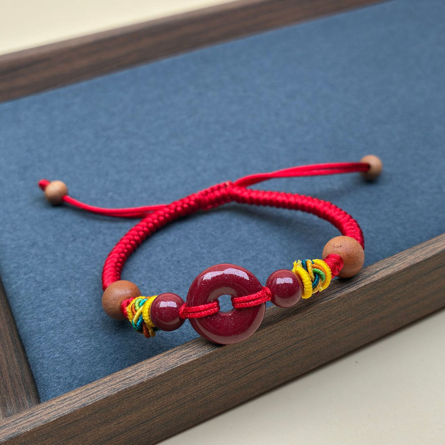 Close up of a red string bracelet with a red peace buckle charm on a wrist