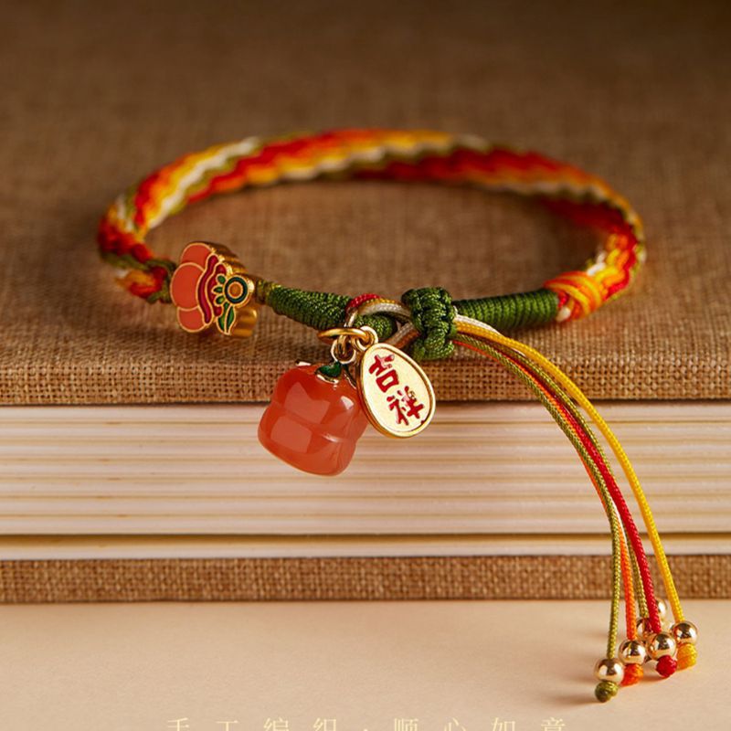 Close up of a red and yellow braided bracelet with a red agate persimmon charm
