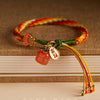 Close up of a red and yellow braided bracelet with a red agate persimmon charm