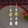 Pair of long drop earrings with a gold-tone chain, a white faux pearl, and a white teardrop charm.