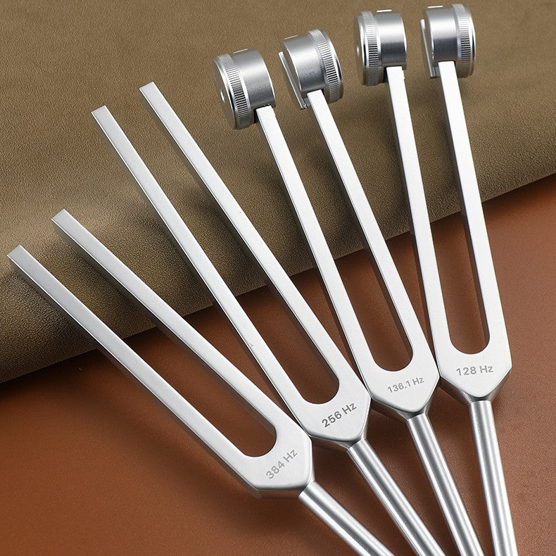 Four silver aluminum alloy tuning forks laid out on a brown surface