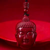 Close-up of a red cinnabar pendant carved in the shape of a Buddha head on a black cord