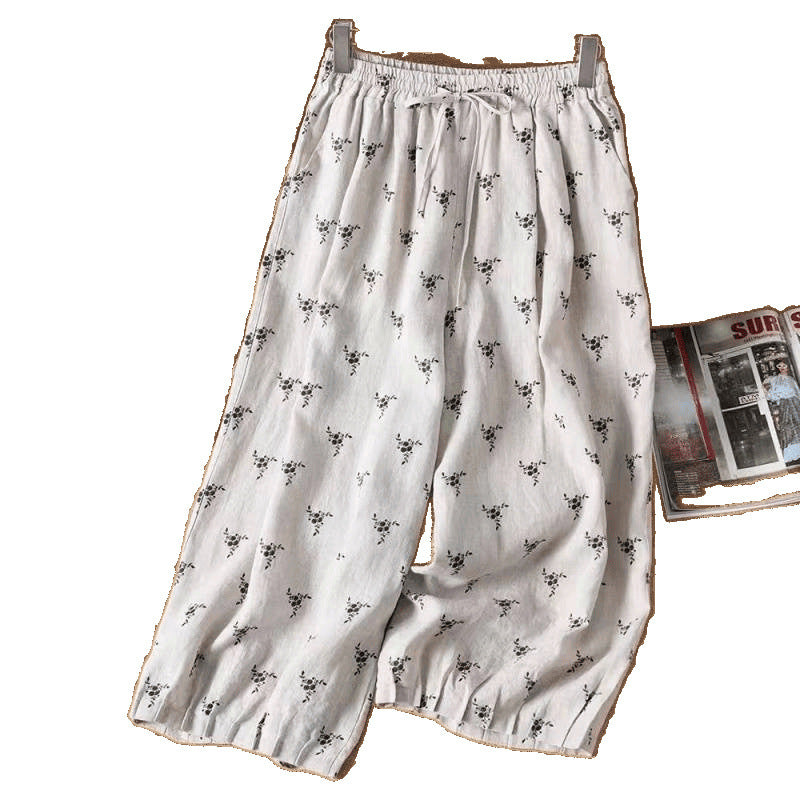 White wide leg linen pants with small black floral print hanging on a wooden hanger