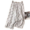 White wide leg linen pants with small black floral print hanging on a wooden hanger