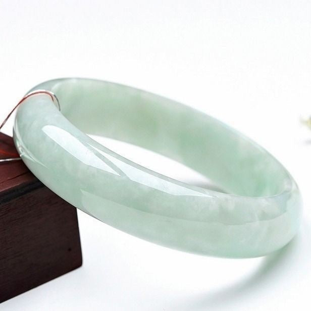 Polished natural jade bangle bracelet resting on a wooden stand