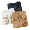 Three folded women's shirts in orange, navy, and white with leaf embroidery details