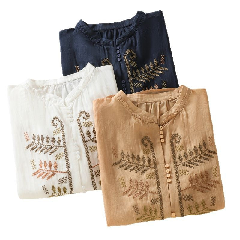 Three folded women's shirts in orange, navy, and white with leaf embroidery details